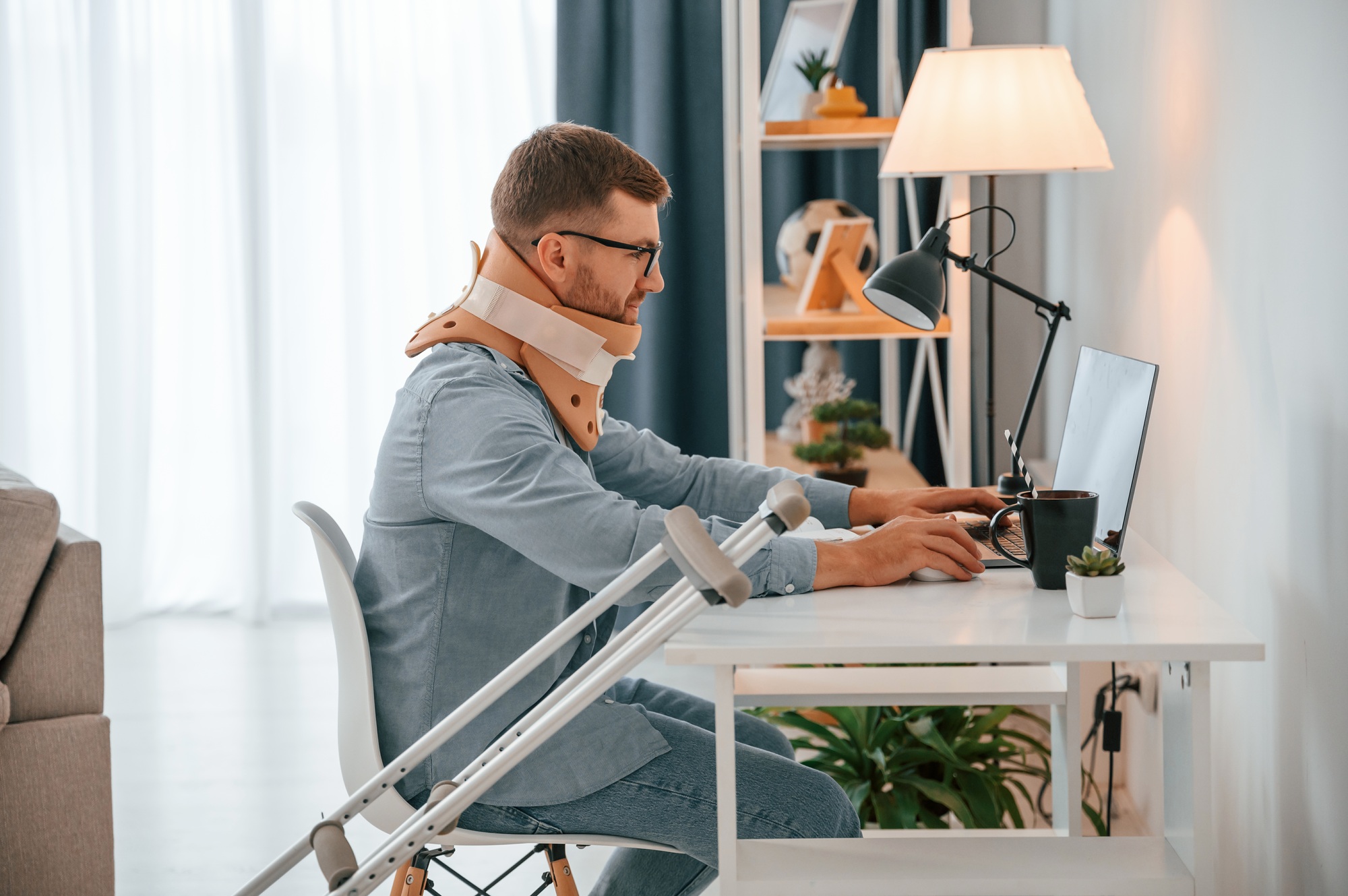 Working from home by using laptop. Man with crutches is indoors. Having injuries